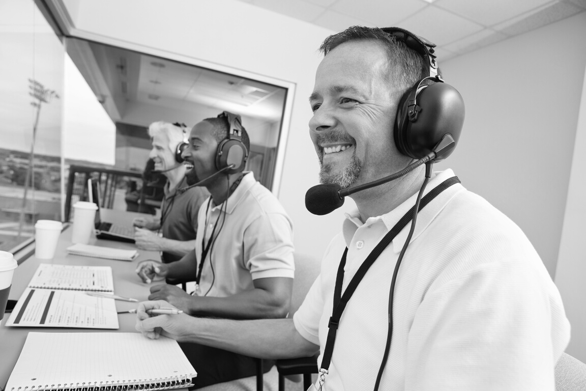 Sports commentators wearing headsets; reporting from stadium press box